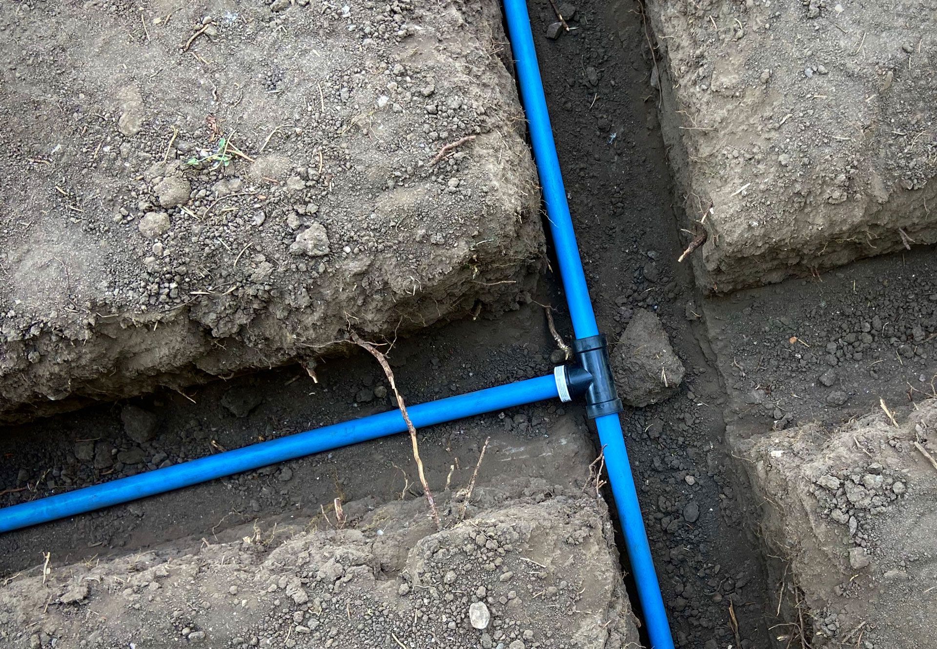 Blue plastic pipes laid in a dirt trench beside concrete blocks