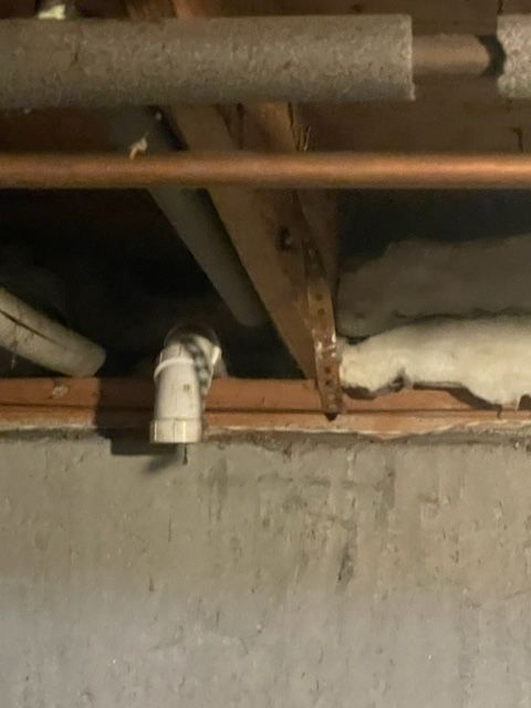View from below of pipes, insulation, and wood in a basement setting.