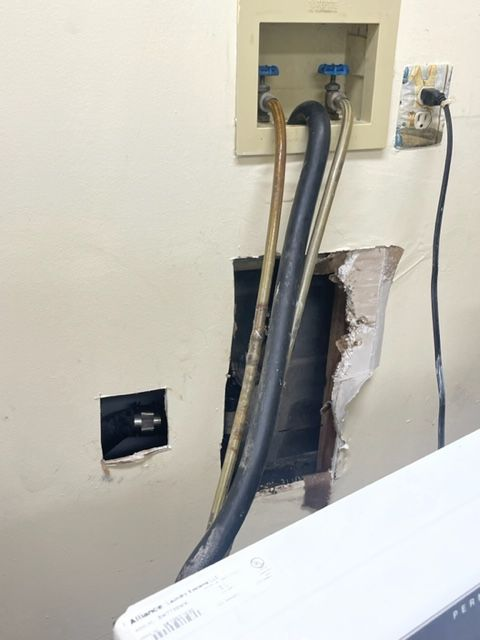 Laundry room with exposed pipes and wall damage around a water supply box.