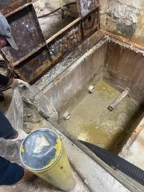 Person near a concrete tank with open metal access, likely for cleaning. Yellow bucket nearby.