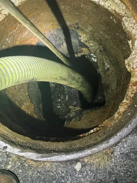A hose extends into a dark, circular sewer drain. The drain is made of concrete with visible wear and tear.