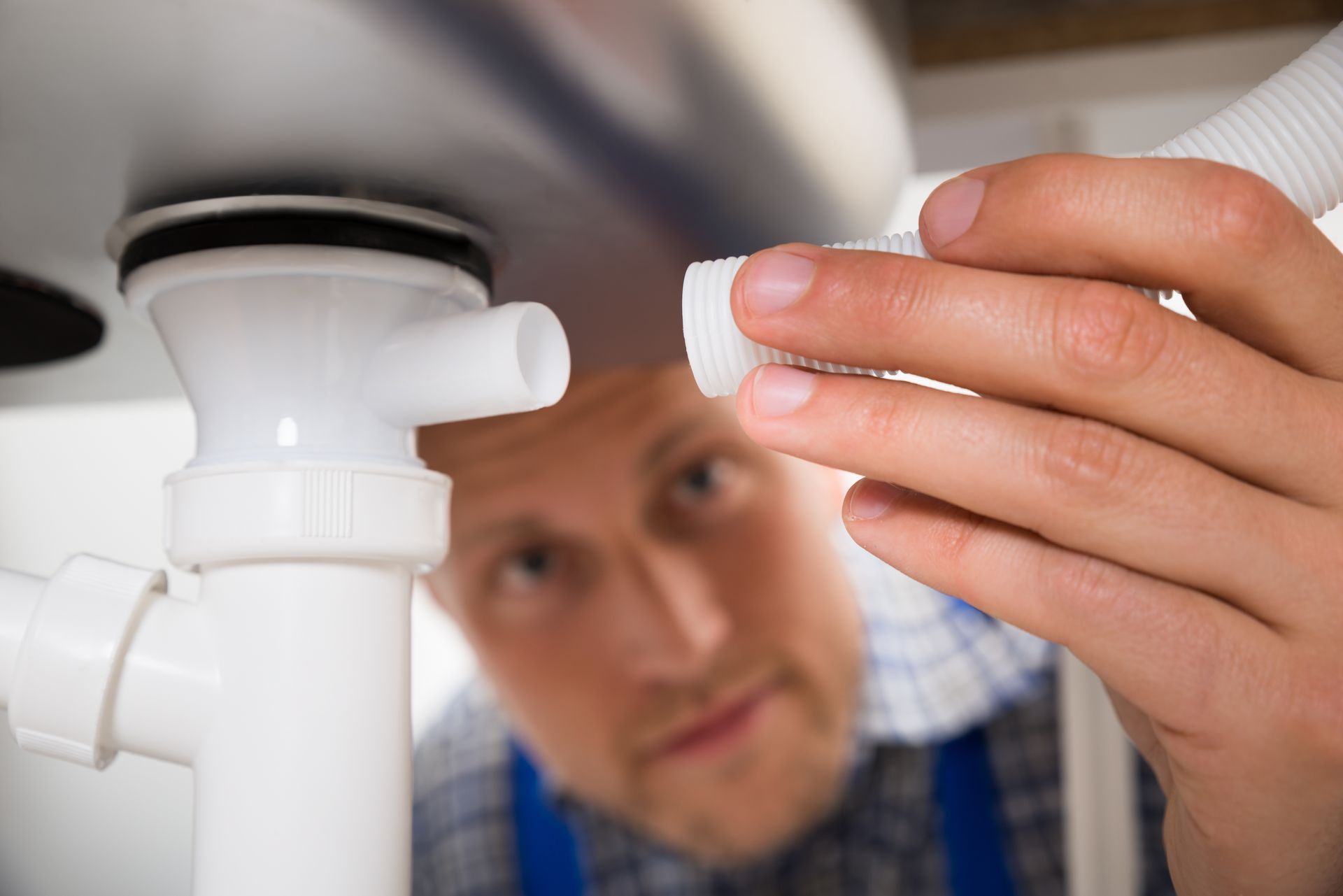 Plumber connecting a white drain pipe under a sink.