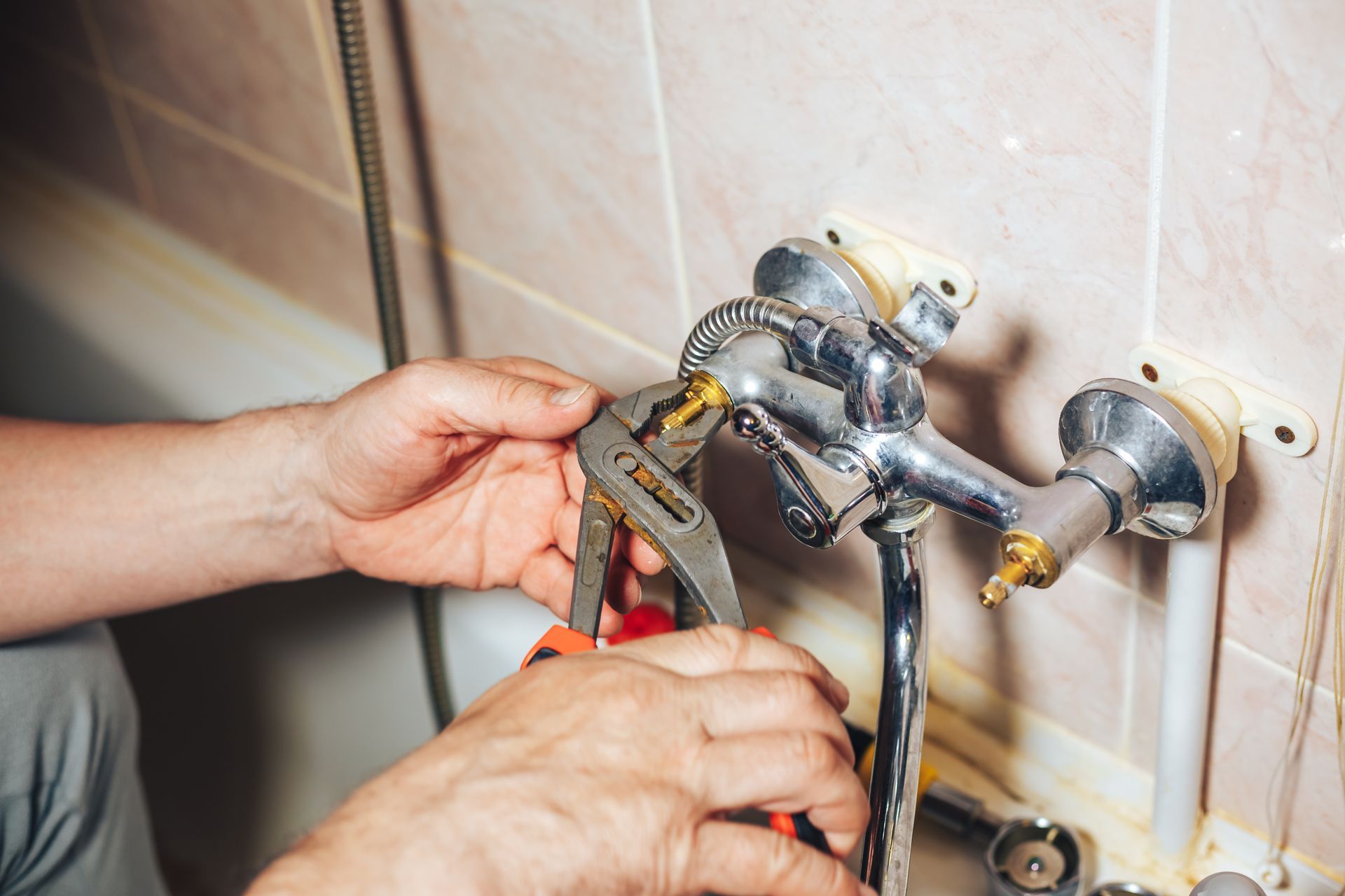 Person using pliers to work on a faucet in a bathroom.