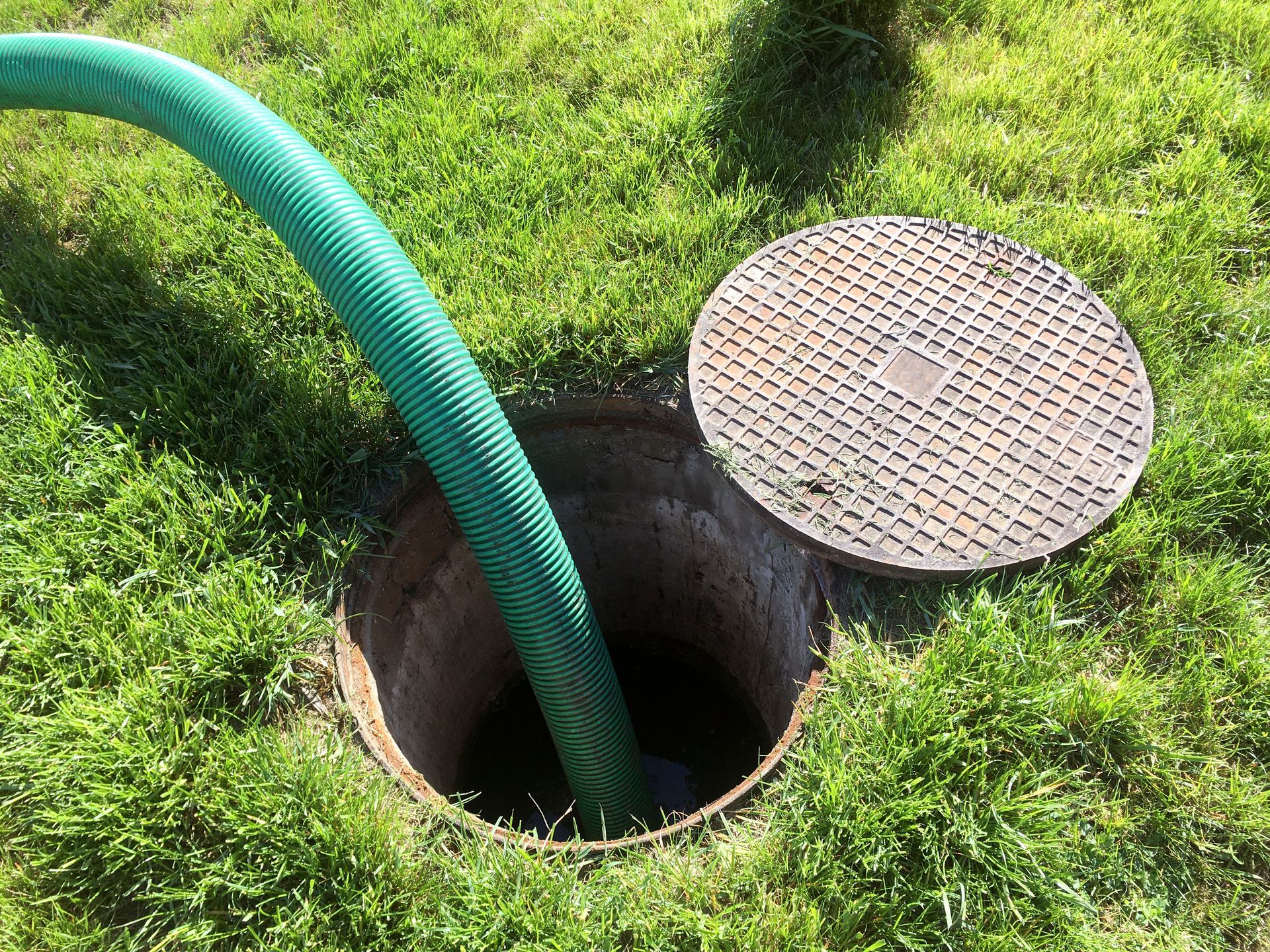 Green hose entering a septic tank opening in grass, lid nearby.