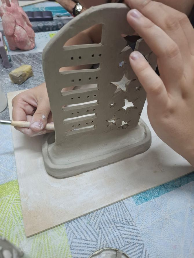 En un espacio de trabajo en un estudio, se elabora a mano un soporte de arcilla para joyas con recortes.