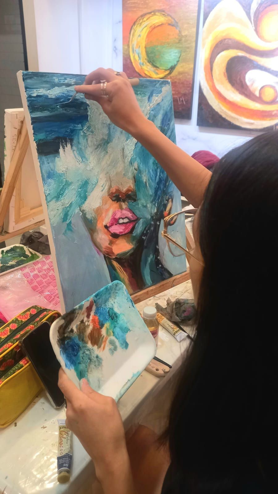Un artista pinta el retrato de un rostro parcialmente oculto por pinceladas azules y texturizadas.