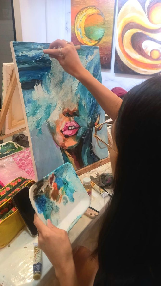 Un artista pinta el retrato de un rostro parcialmente oculto por pinceladas azules y texturizadas.