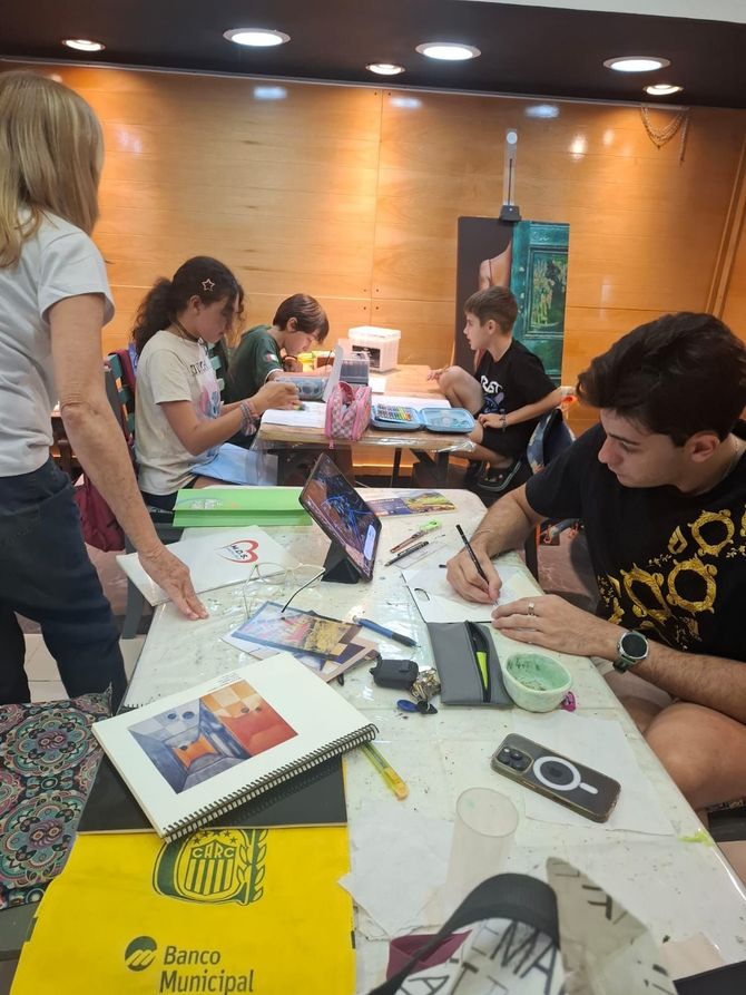 Un grupo de personas dibujando en una mesa larga en una habitación con iluminación cálida y paredes revestidas de madera.