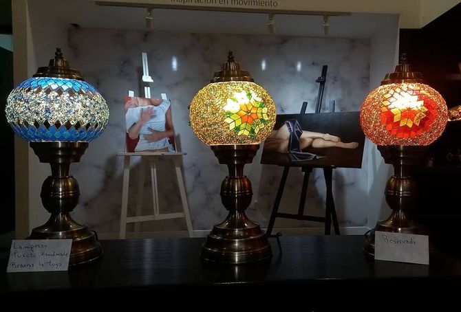 Tres lámparas de cristal con mosaicos ornamentados en azul, dorado y rojo brillan sobre una estantería oscura.