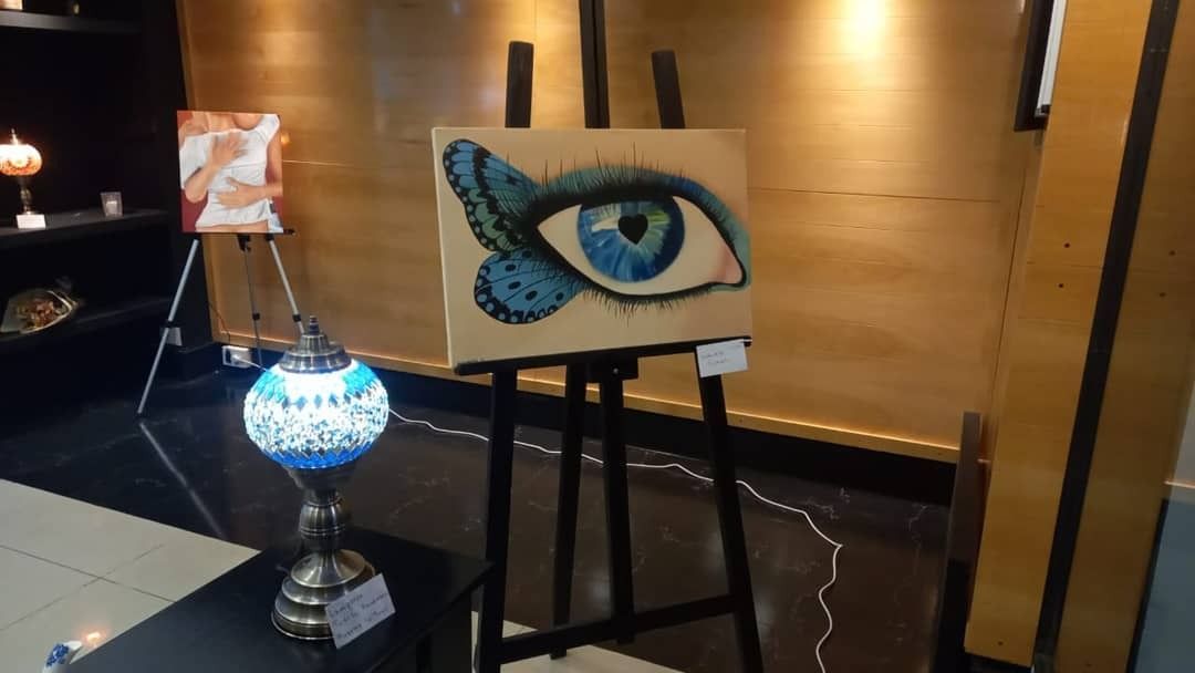 Cuatro personas crean arte en un estudio luminoso con grandes ventanales, caballetes de madera.