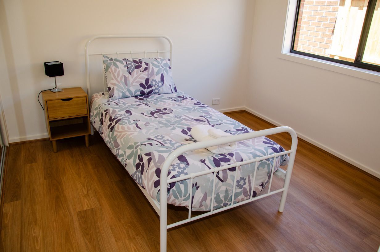 A bedroom with a single bed , nightstand , and window.