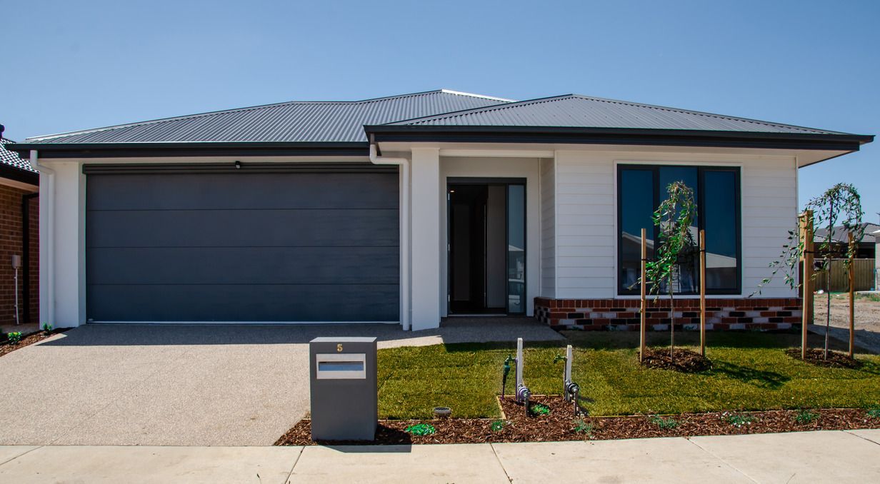 A white house with a black garage door and a mailbox in front of it.