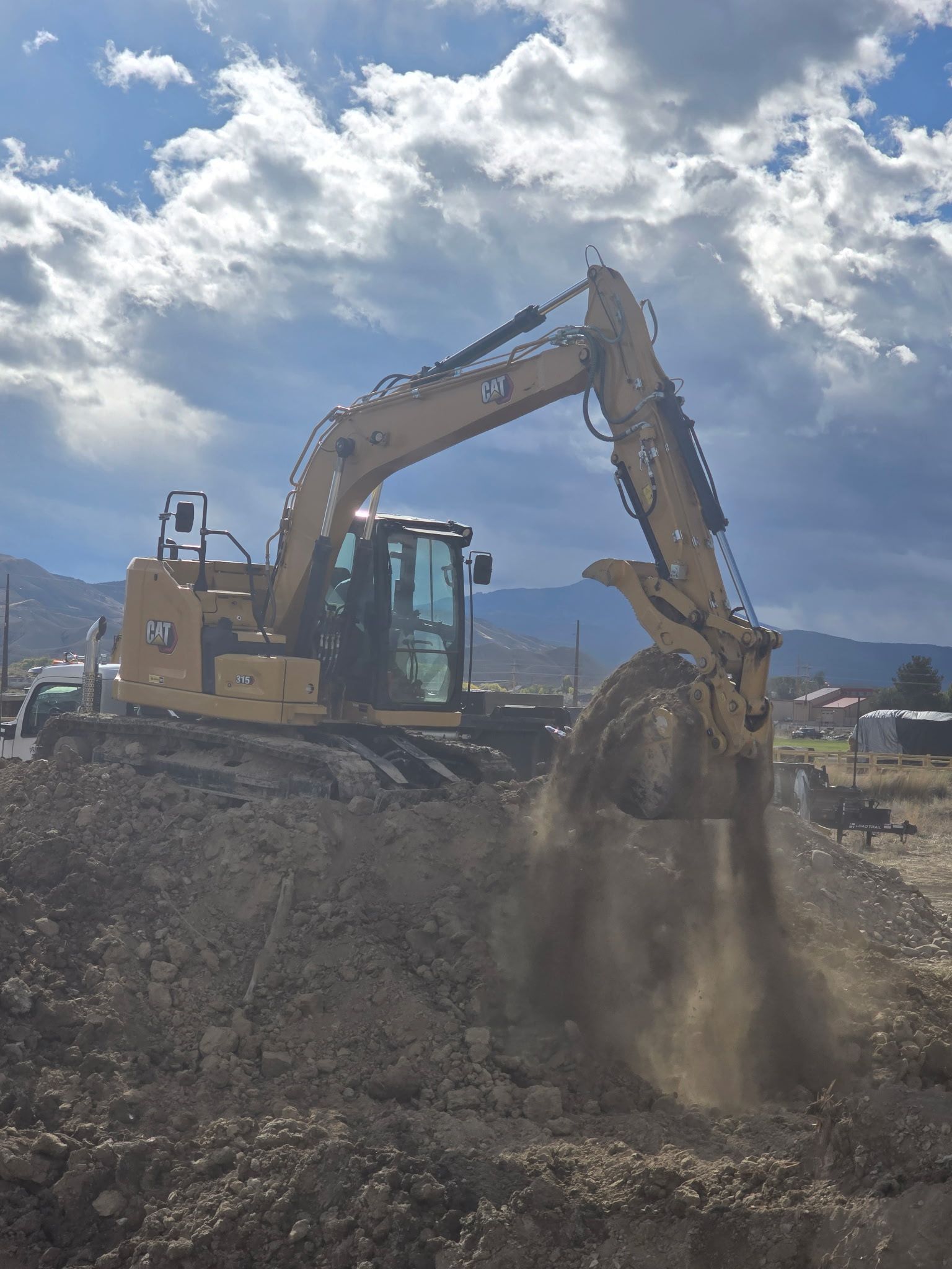 Yellow excavator digging into a pile of dirt under a cloudy sky.