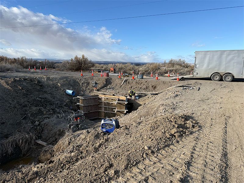 Construction site: Workers building a structure in a large dirt excavation. Trailer and traffic cones present.