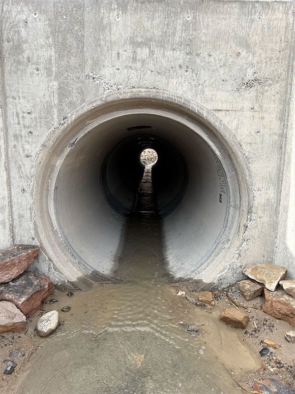 Concrete tunnel with water flowing through, opening to a distant light.