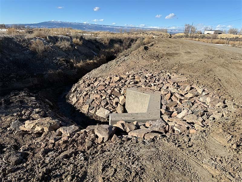A carved concrete monument at the bottom of an excavated, rocky ditch. Brown earth and distant mountains.