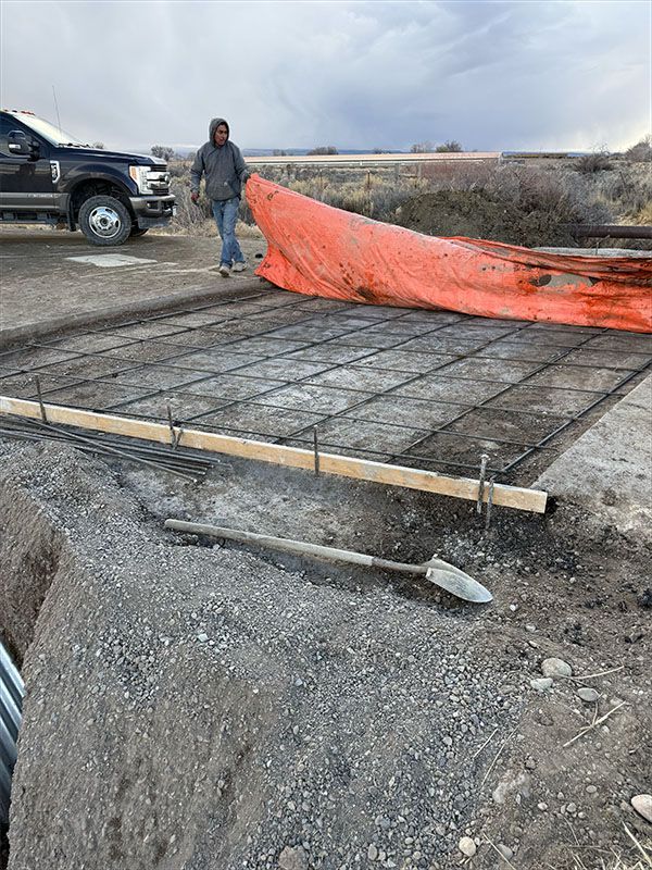 Construction site with worker, rebar grid, and orange tarp. Outdoor setting with truck.