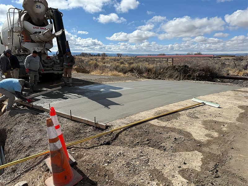 Workers pouring concrete from a truck to create a new concrete slab outdoors under a blue sky.