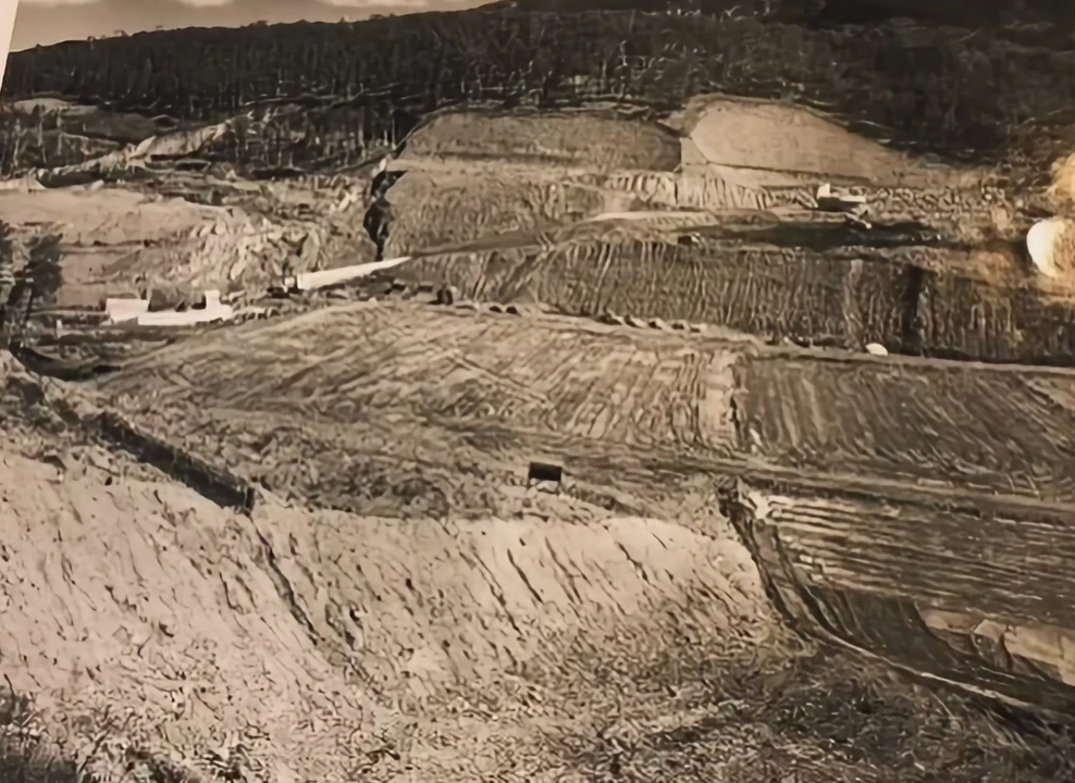 A black and white photo of a dirt field with trees in the background