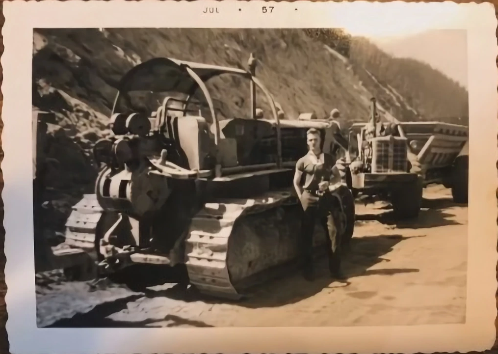 A black and white photo of a man standing next to a bulldozer