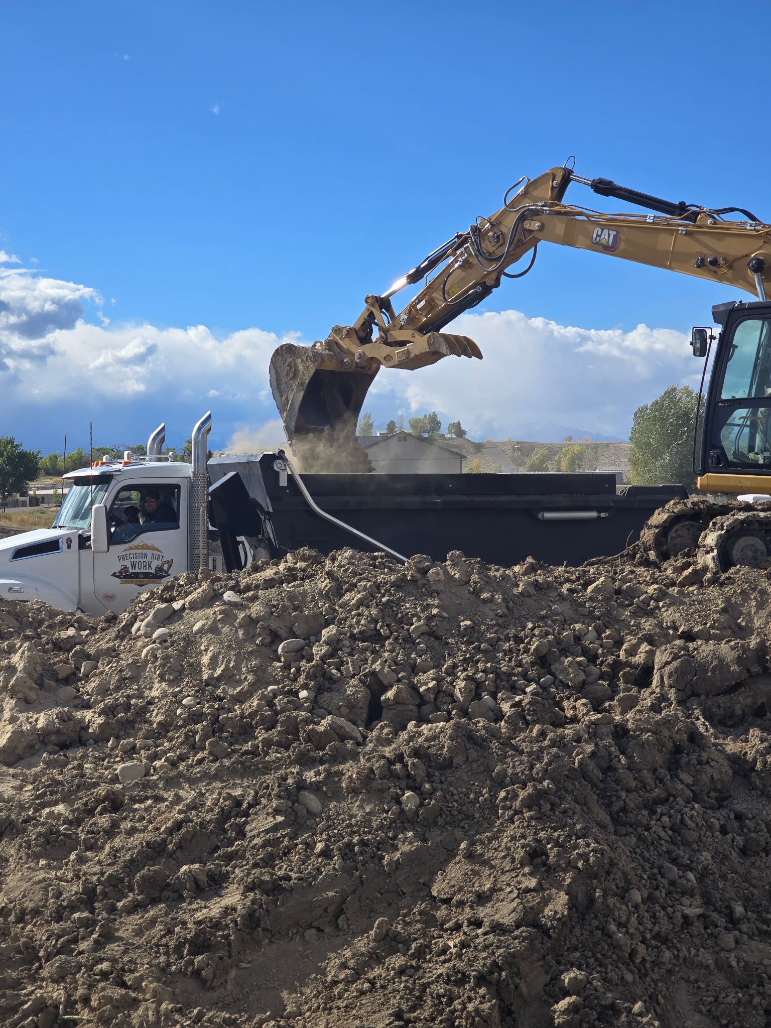 An excavator loading a dump truck with dirt on a sunny day.