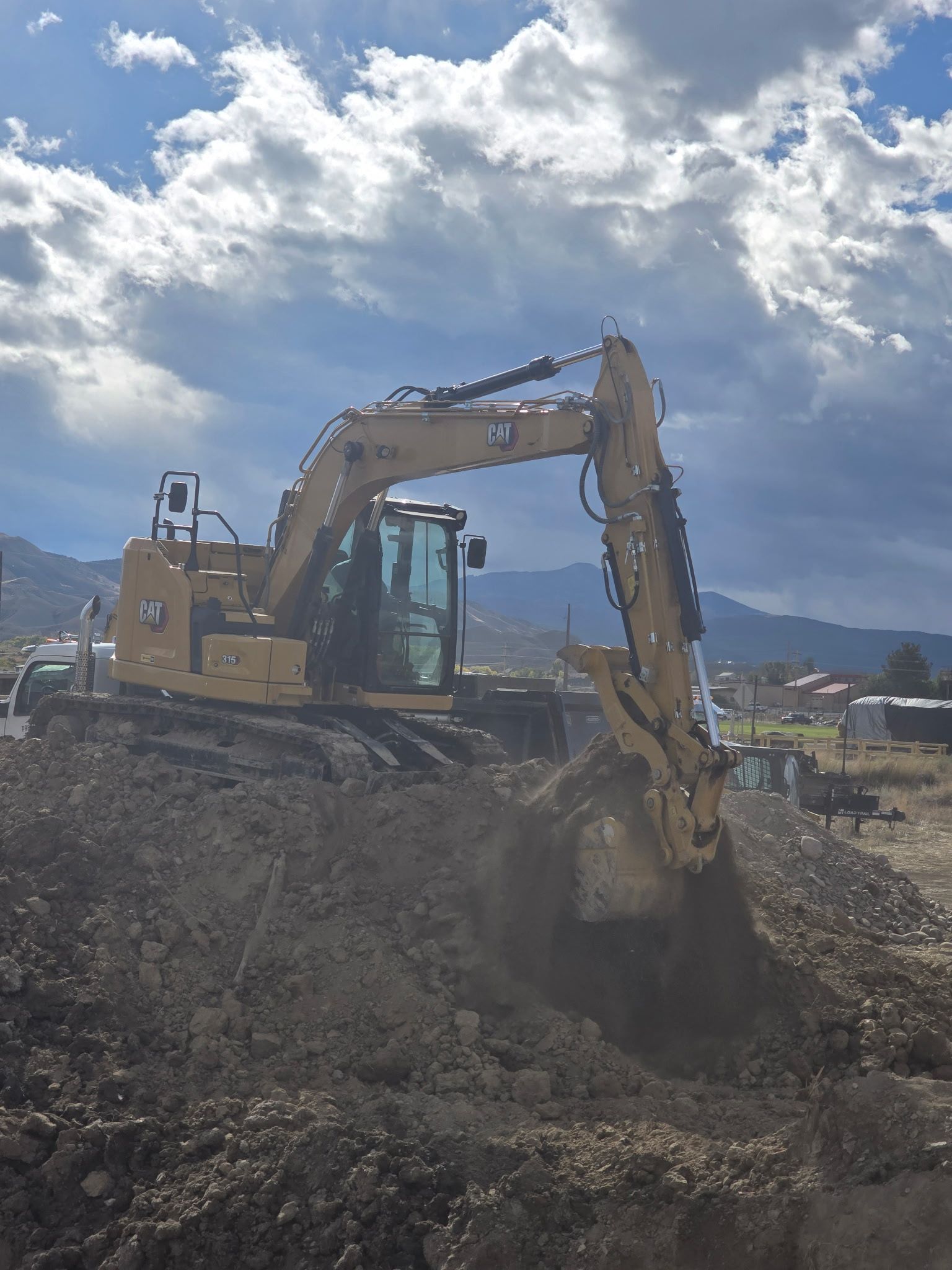 Yellow Caterpillar excavator digging in dirt under a cloudy sky.