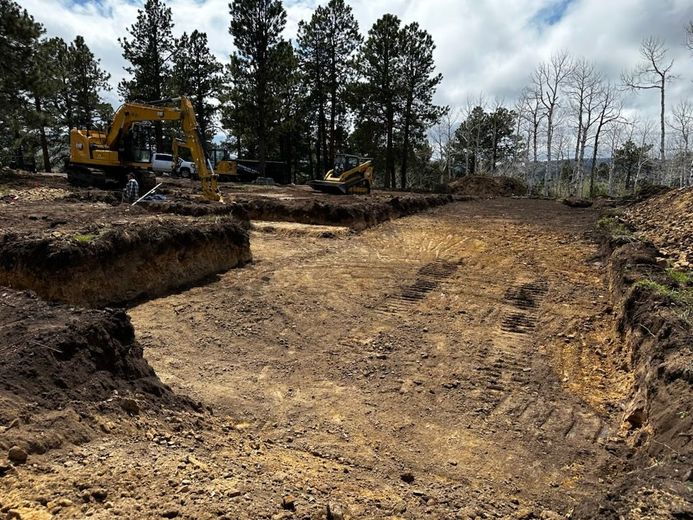 A yellow excavator is digging a hole in a dirt field.