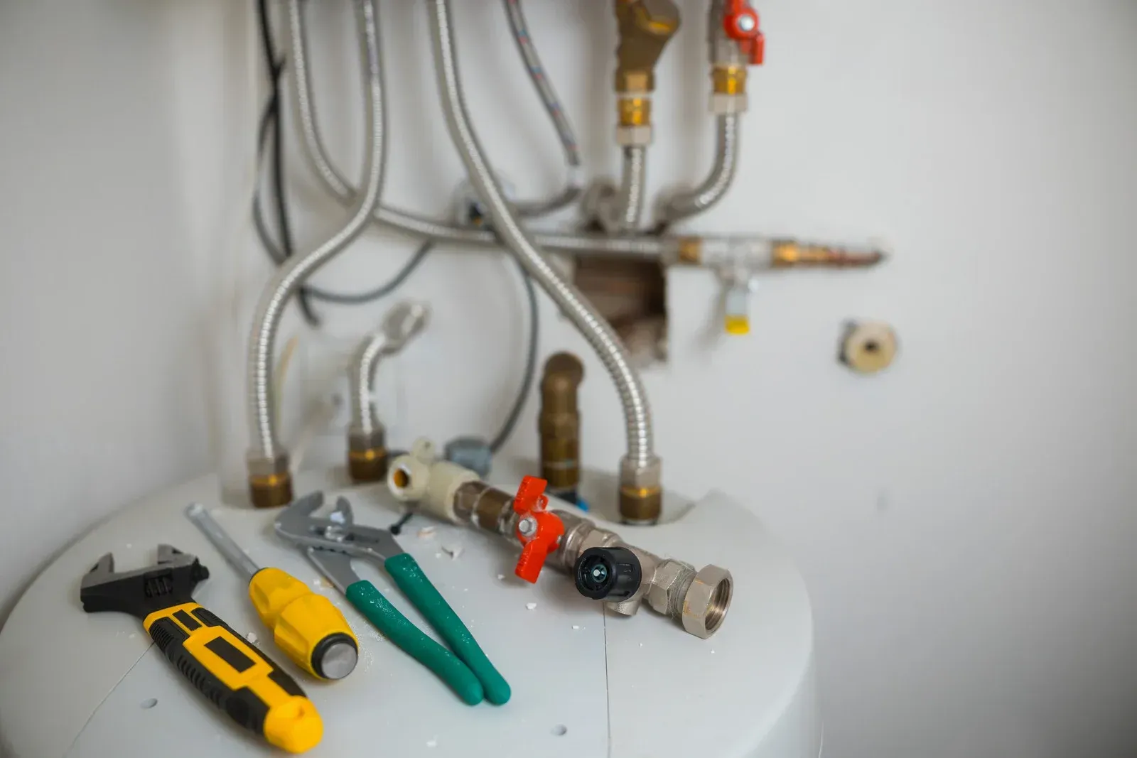 Tools on top of a water heater; plumbing pipes and valves are visible, white wall background.