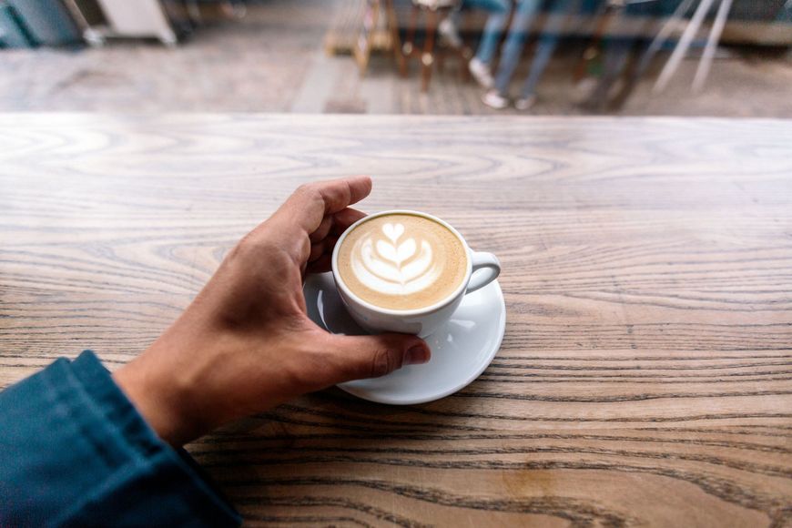 una persona tiene in mano una tazza di caffè su un tavolo di legno