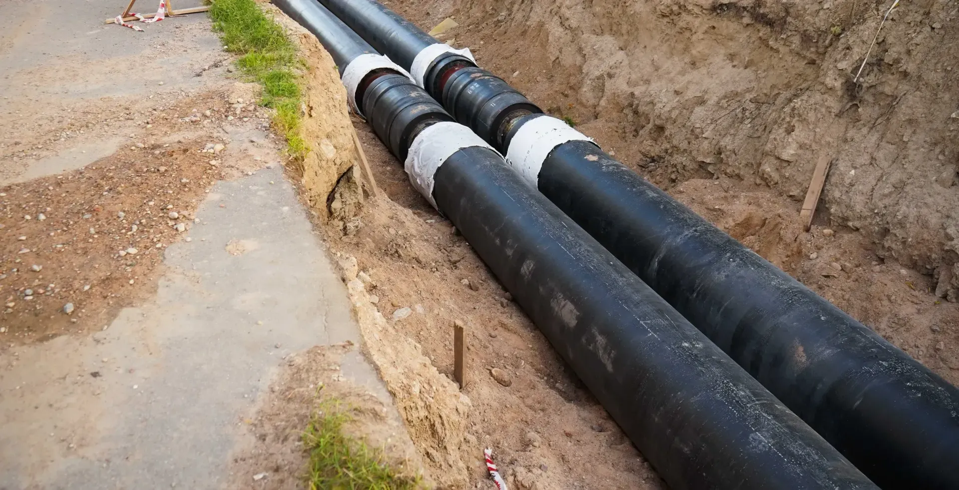 Two black pipes installed in a trench next to a paved surface.
