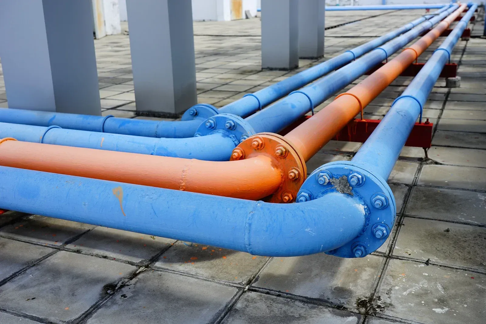 Gray corrugated metal wall with black pipes and a textured black walkway with white circular markers.