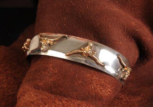 Silver and gold-tone cuff bracelet with three bull head accents on a brown fabric background.