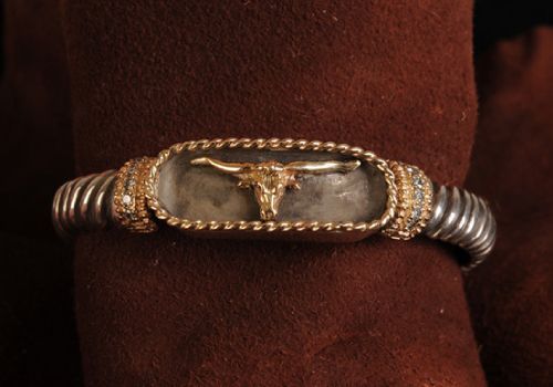 Silver bracelet with gold bull horns, set against brown material.