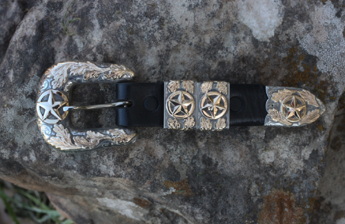 Silver and black belt buckle with stars and floral accents on a rock.