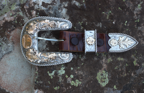 Silver and gold Western belt buckle on a brown leather belt, set on a rock.