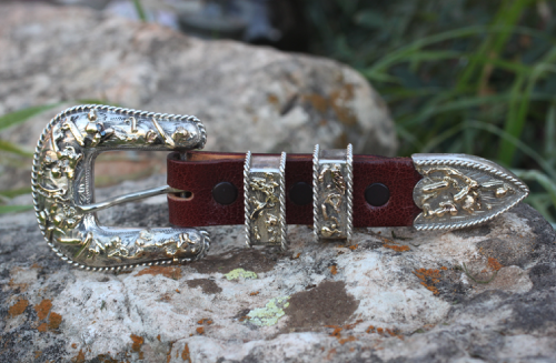 Silver and brown western belt buckle set resting on a rock.