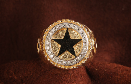 Gold ring with black star, surrounded by diamonds, on brown fabric.