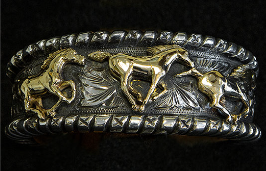Silver and gold cuff bracelet with three golden horses galloping across it.