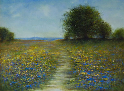 A path through a wildflower field leads to distant trees under a hazy blue sky.