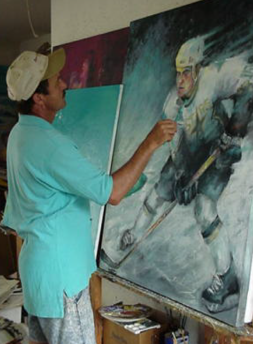 Artist paints a hockey player on a large canvas, wearing a light blue shirt and a baseball cap.