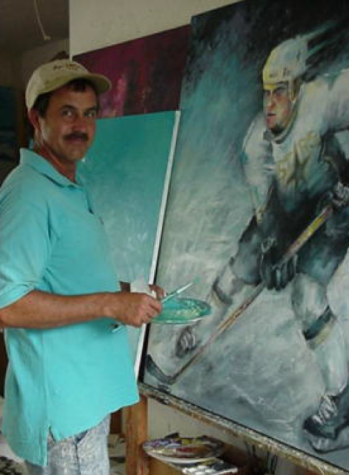Artist painting a hockey player; wearing a hat, holding a palette, standing in front of the canvas.
