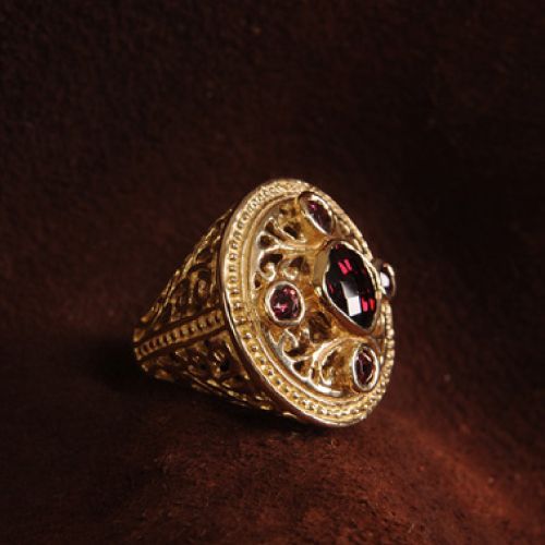 Gold ring with ornate filigree design, set with dark red gemstones.