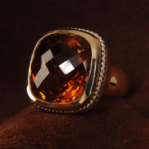 Gold ring with a large, faceted, amber-colored gemstone set in a textured, gold frame.