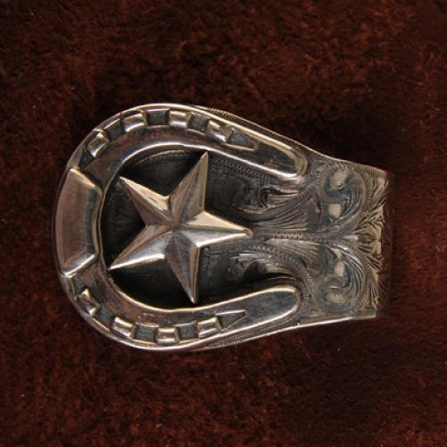 Silver horseshoe-shaped belt buckle with star and floral engraving on a brown background.