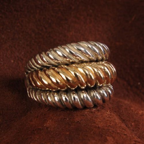Three twisted metal rings, two silver and one gold, stacked on brown leather.