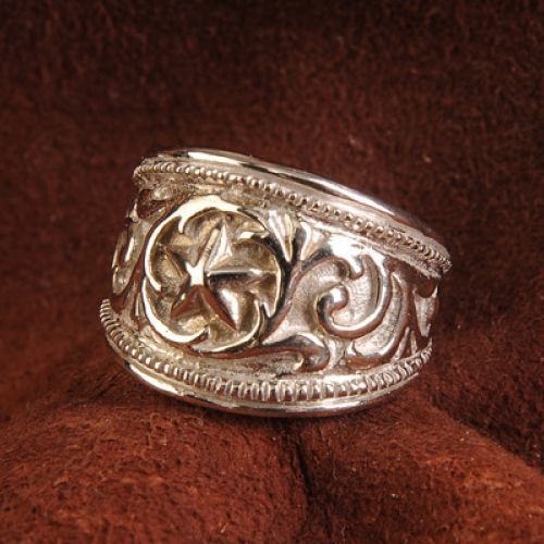 Silver ring with a star design and ornate scrollwork on a brown background.