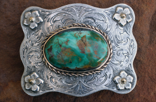 Silver belt buckle with a turquoise stone and floral accents.