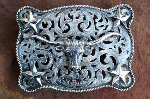 Silver belt buckle with a Texas longhorn, stars, and ornate scrollwork.