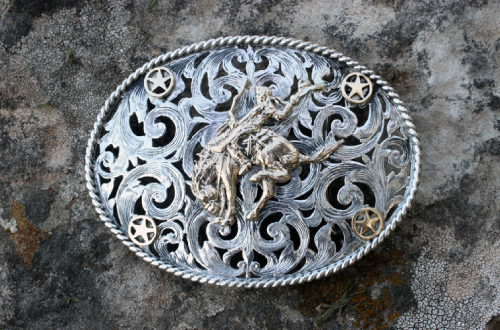 Silver cowboy belt buckle featuring a rodeo rider and star accents, on a textured background.