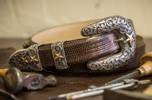Silver and gold detailed belt with a star buckle, sitting on a work surface with tools.